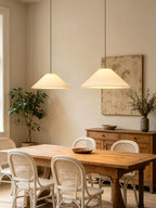 Two beige Clérachic cone pendants hang above a reclaimed-wood table flanked by woven rattan chairs.