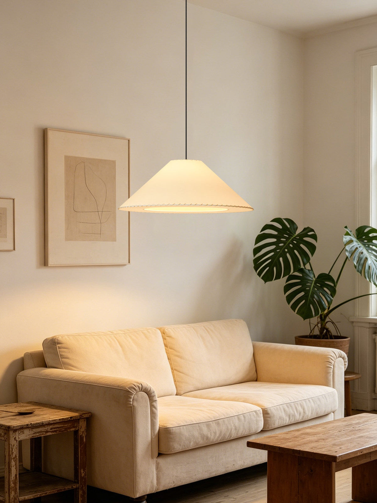 Beside a cream sofa and a leafy potted plant, a beige Clérachic pendant glows in a living room corner.