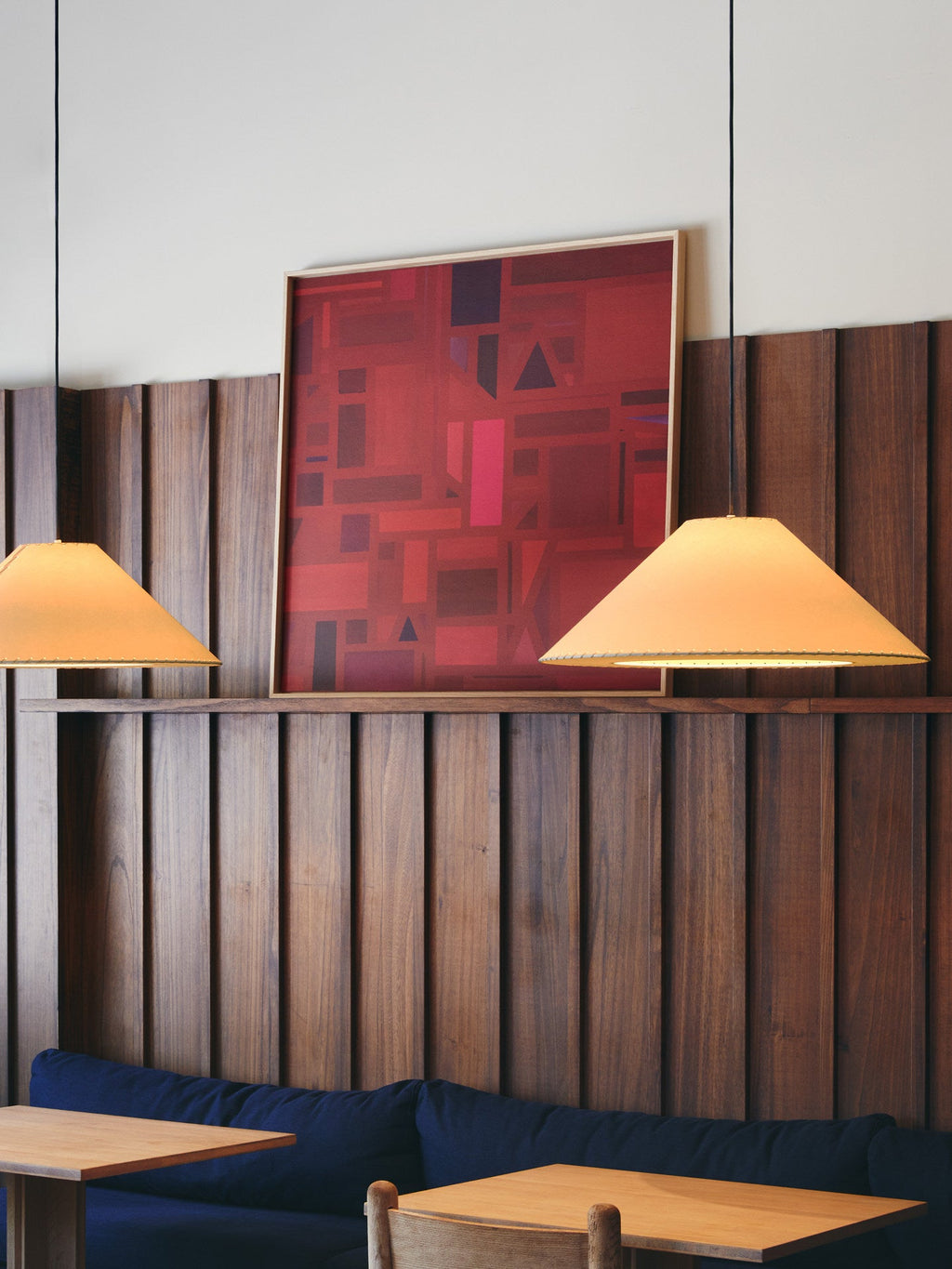 Two beige Clérachic cone pendants hang against a wood-panelled wall beside a navy banquette.