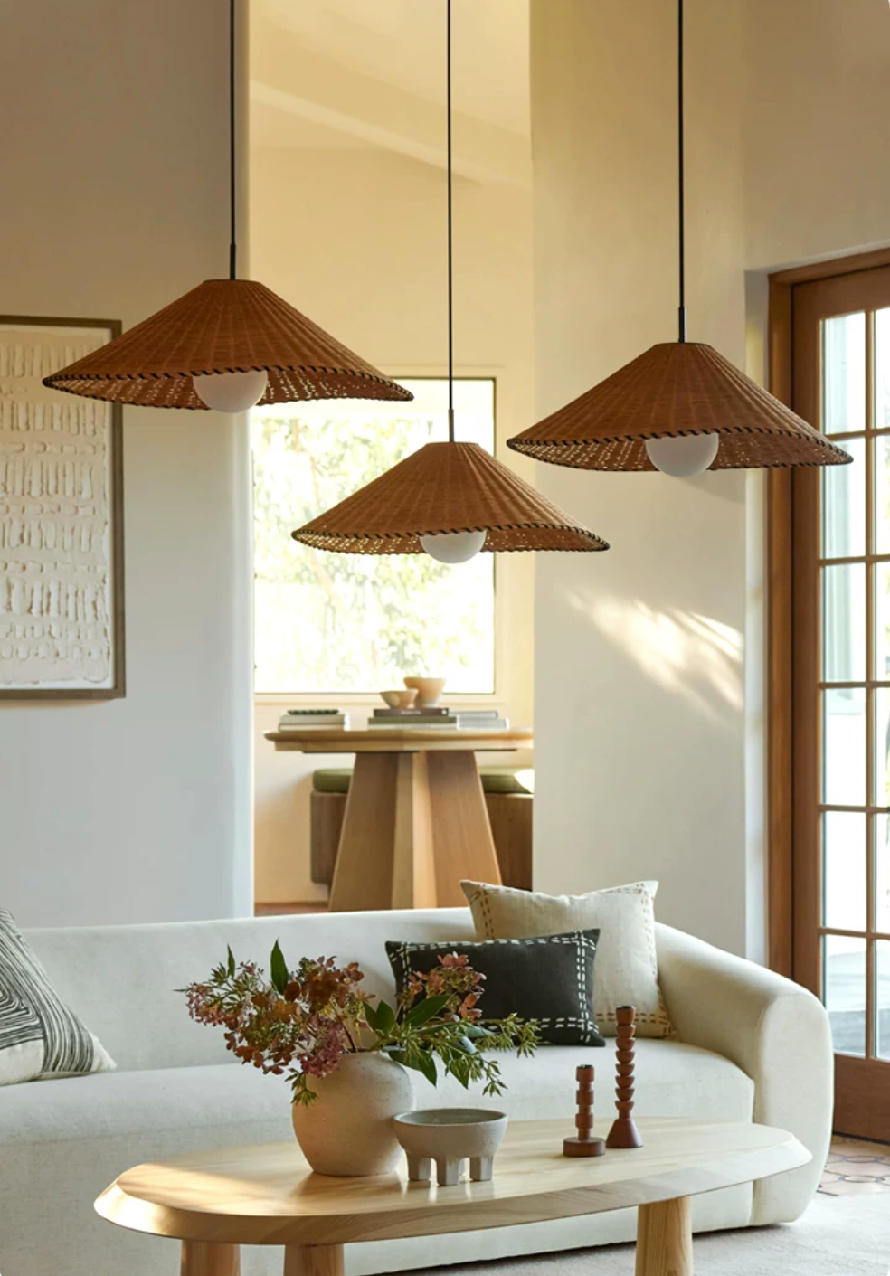Two sizes of this Clérachic pendant hang lit at staggered heights above a coffee table near glass doors.