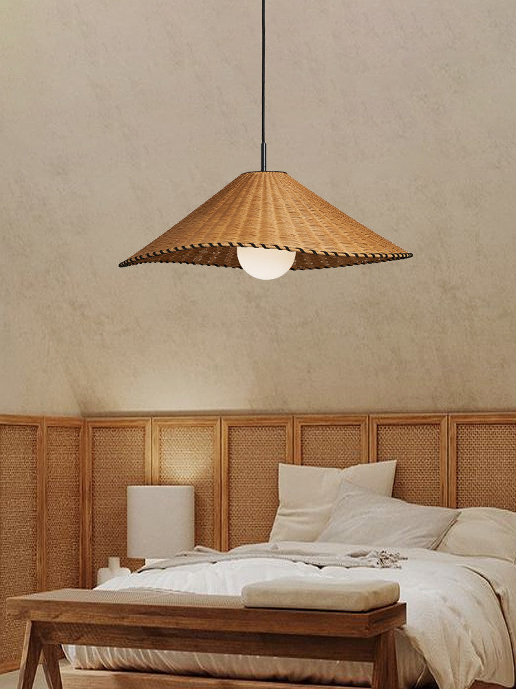 A cane headboard and a wood bench sit beneath this lit Clérachic pendant in a bright bedroom.