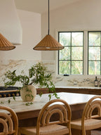 Two sizes of this Clérachic pendant hang lit above a wood table with cane chairs near a marble backsplash.