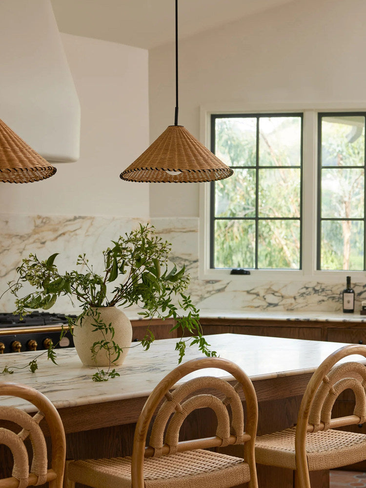 Two sizes of this Clérachic pendant hang lit above a wood table with cane chairs near a marble backsplash.