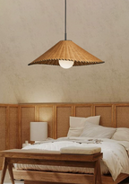 Beside a wood bench and cane headboard, this lit Clérachic pendant hangs in a bright bedroom.