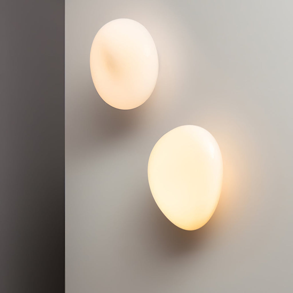 Translucent pebble glass wall lamp lit warm white on a wall