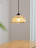 This Clérachic pendant hangs lit above a wood table, a green leaf blurred in the foreground.