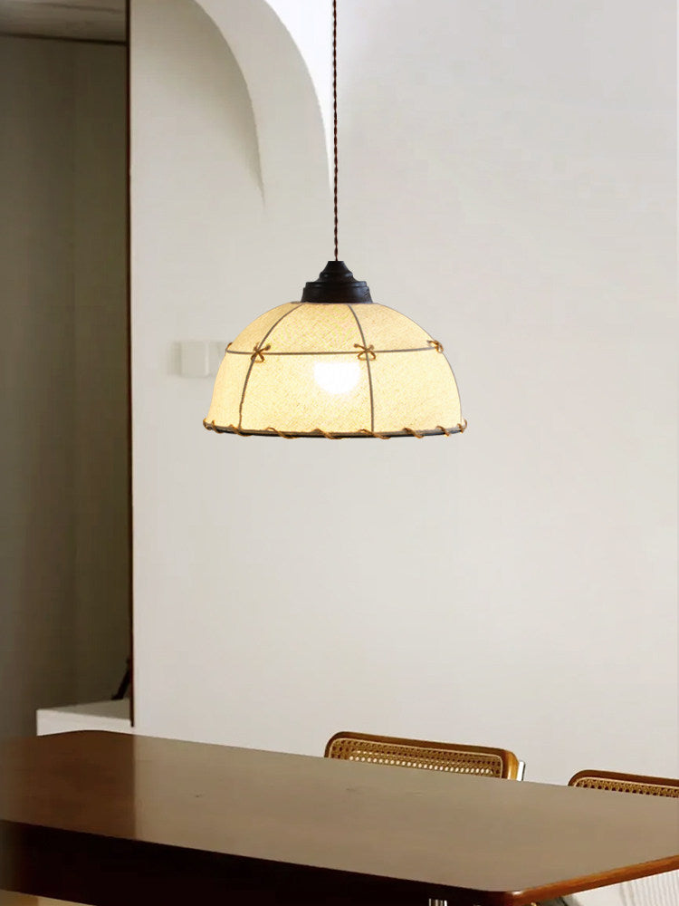 Beneath an archway near a dining table, this Clérachic pendant's quilted beige shade glows softly.