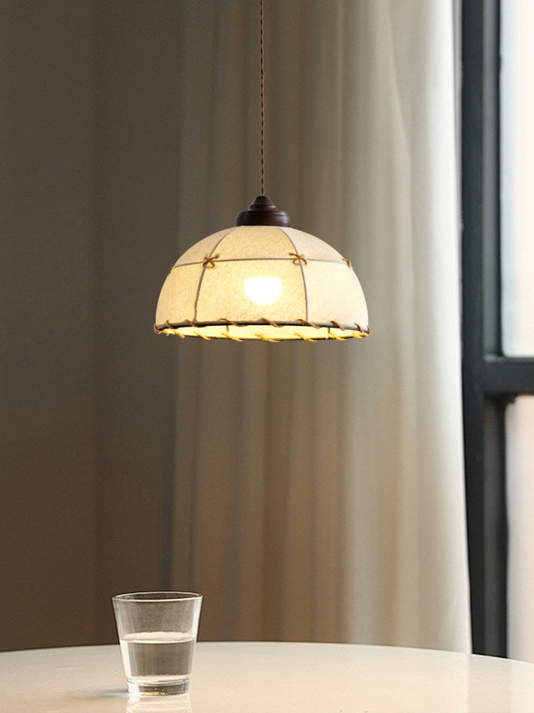 Beside a curtained window, this Clérachic pendant hangs lit above a table holding a single glass of water.