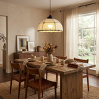 Between sheer curtains, this Clérachic pendant hangs lit above a wood dining table set for a meal.