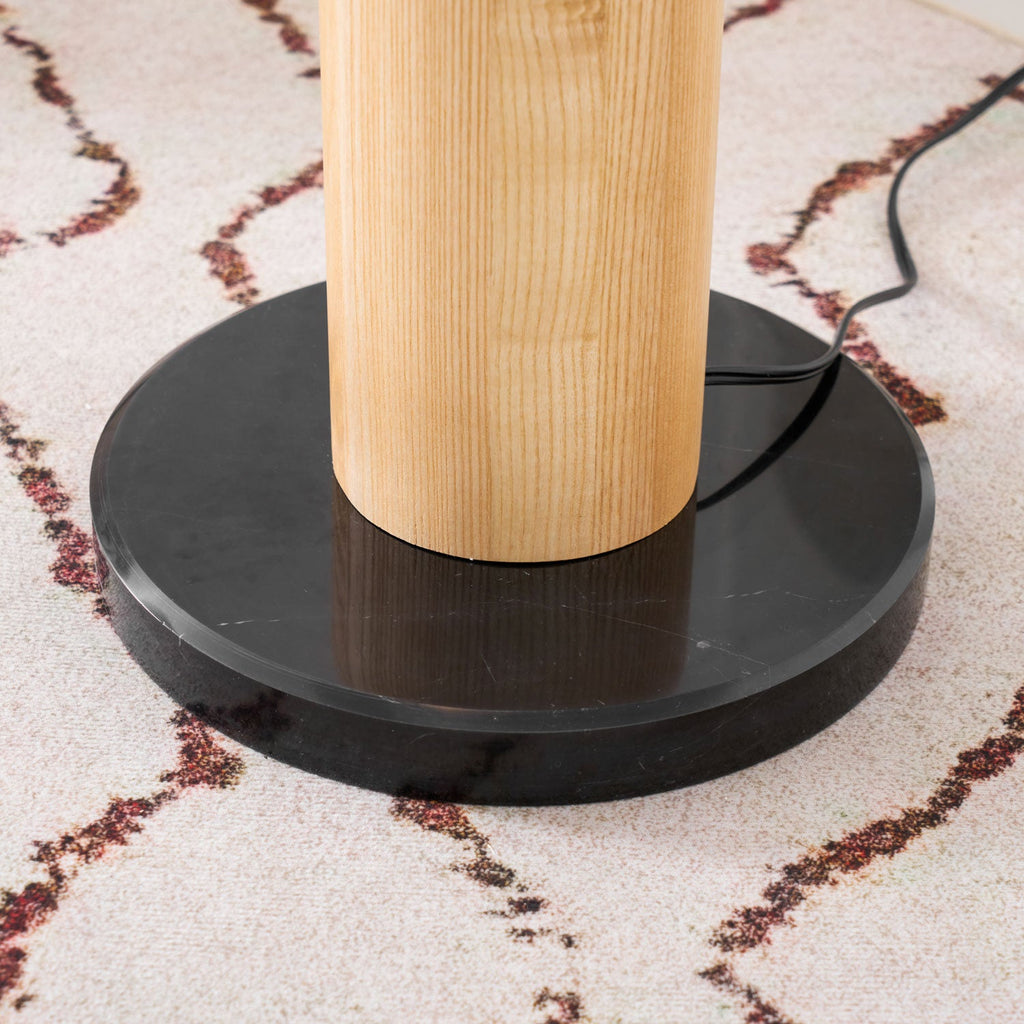 Extreme close-up of a Clérachic floor lamp's round black marble base and cord resting on a patterned rug.