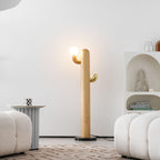 Clérachic floor lamp with a warm glass globe lit on its brass branch, the curved wood column standing tall against a plain white wall.