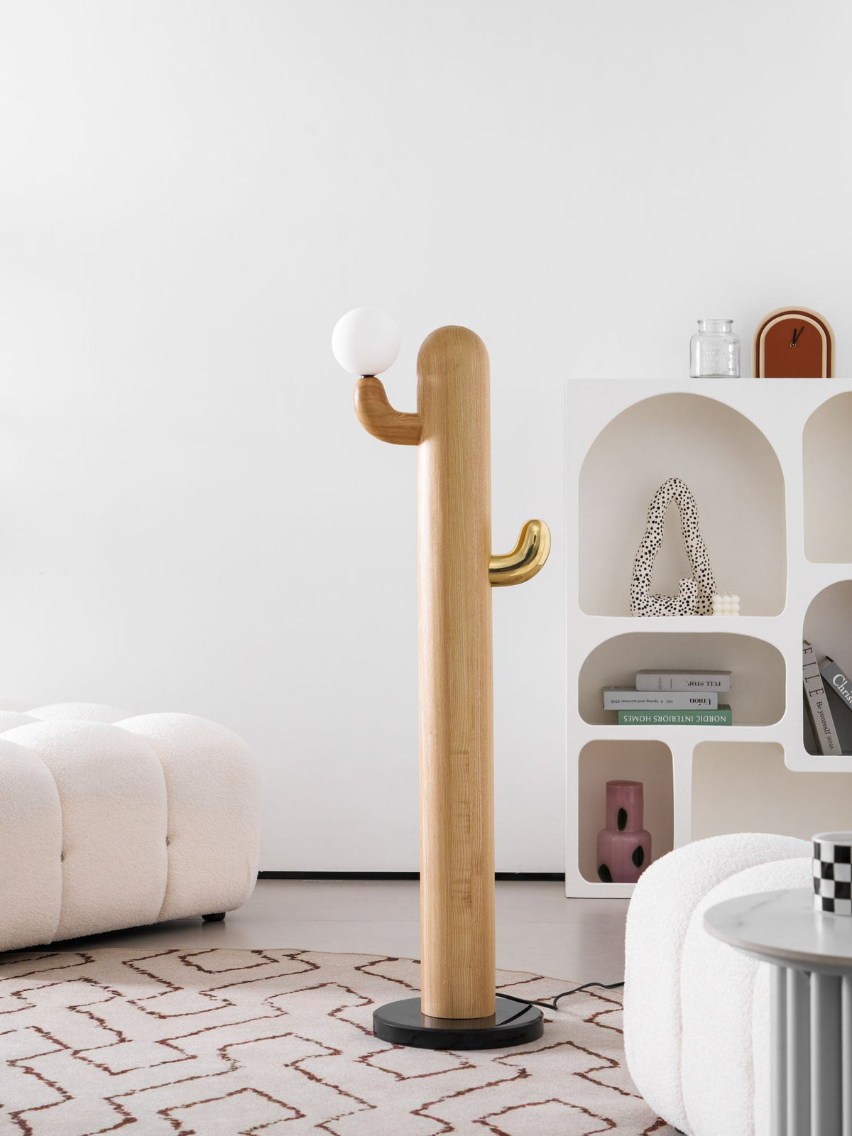 Clérachic wood floor lamp seen from a slightly lower angle, its lit glass globe bright against the soft-focus bookshelf and ottoman.