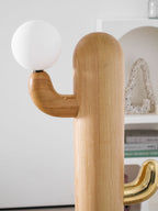 Close-up of a Clérachic floor lamp's pale wood grain shows the brass hook cradling the lit glass orb bulb.