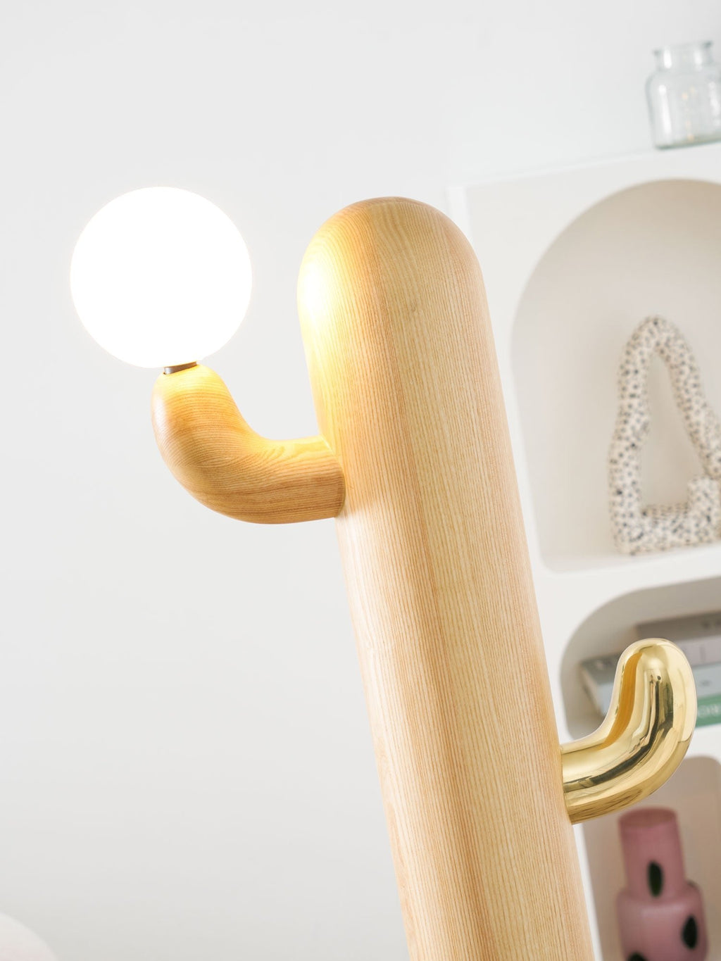 Close-up of a Clérachic floor lamp's pale wood arm reaching toward the glass orb, angled differently than nearby frames.