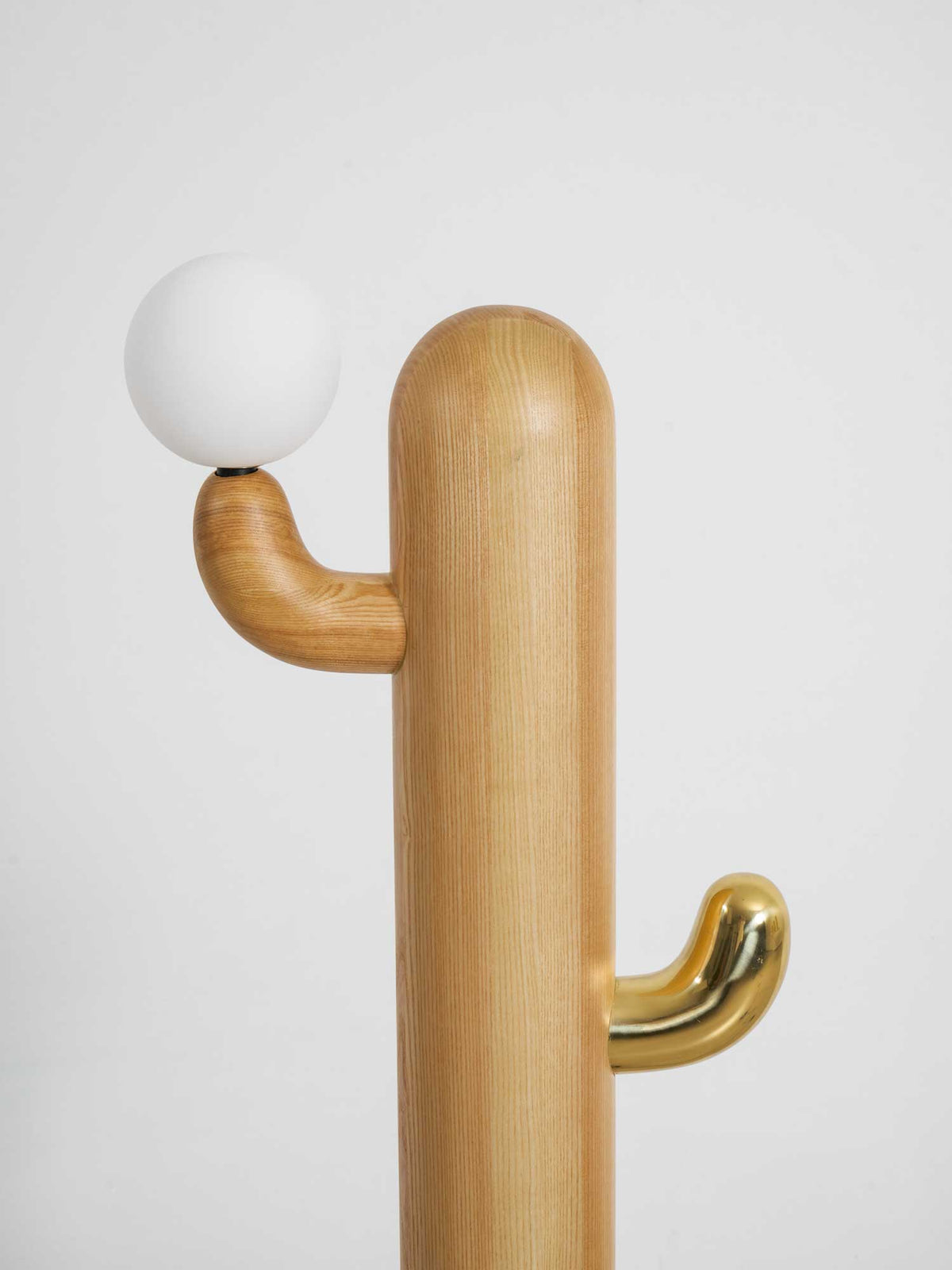 Extreme close-up of a Clérachic floor lamp's pale wood arm cradling the glass orb, brass hook visible below.