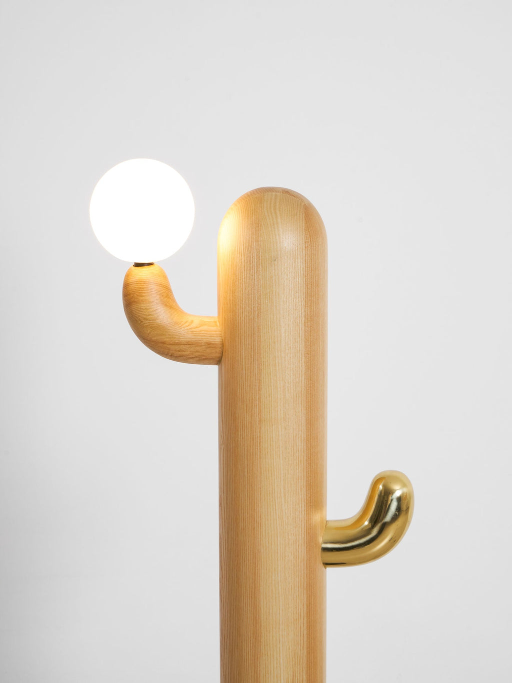 Close-up of a Clérachic floor lamp's brass hook cradling the glass orb, photographed from a lower angle.