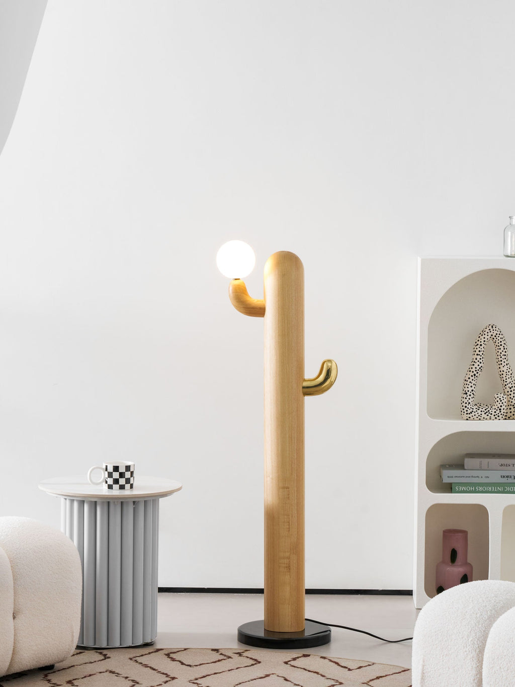 Pale-wood Clérachic floor lamp lit beside a small round side table with a mug, near an arched bookshelf.