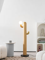 Pale-wood Clérachic floor lamp lit beside a small round side table with a mug, near an arched bookshelf.