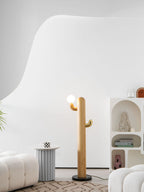 Clérachic branching wood floor lamp with an unlit glass globe on its brass hook, standing near a scalloped bookshelf and cream boucle poufs.