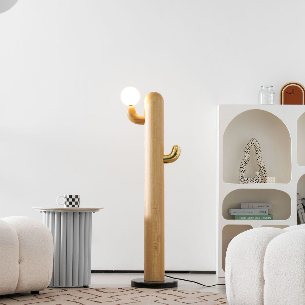 Clérachic wood floor lamp glowing warm from its brass-cradled glass globe, positioned beside an arched bookshelf stacked with books and glass jars.