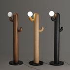 Three Clérachic floor lamps in walnut, pale wood and black finishes stand lit together on a grey studio backdrop.