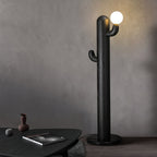 Black Clérachic floor lamp glows against a grey wall beside a dark round coffee table stacked with books.