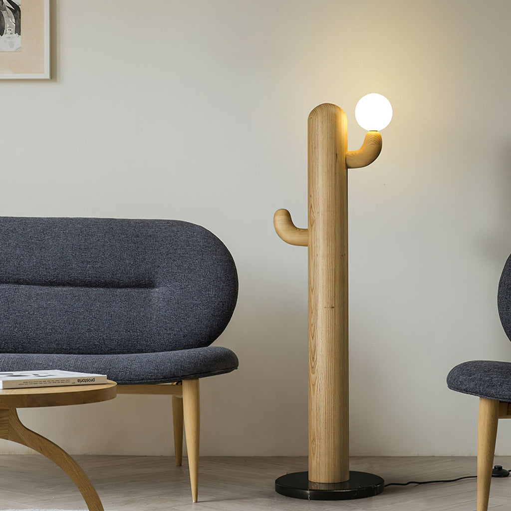Light wood Clérachic floor lamp with a lit glass orb stands beside a curved navy sofa and round wood coffee table.