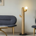 Light wood Clérachic floor lamp with a lit glass orb stands beside a curved navy sofa and round wood coffee table.