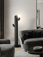 Black-finished Clérachic floor lamp glows beside a curved grey sofa with dark cushions, seen from a wider angle.