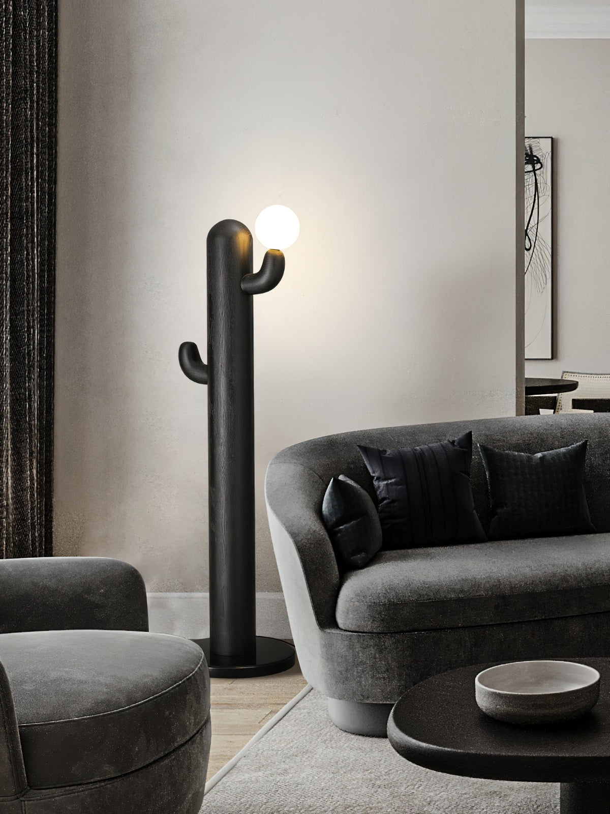 Black-finished Clérachic floor lamp glows beside a curved grey sofa with dark cushions, seen from a wider angle.