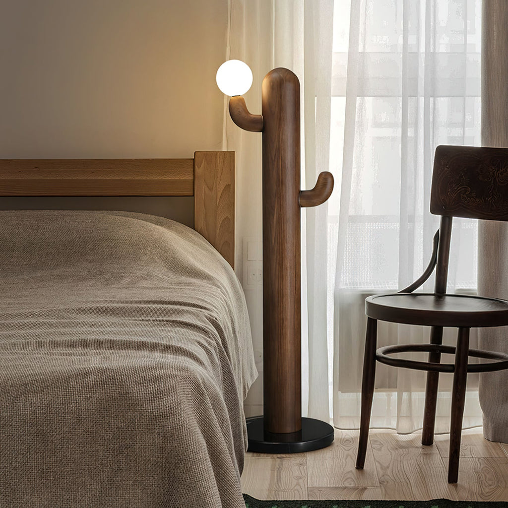 Warm wood-toned Clérachic floor lamp stands beside a wooden bed frame and sheer curtain, its glass orb glowing softly.