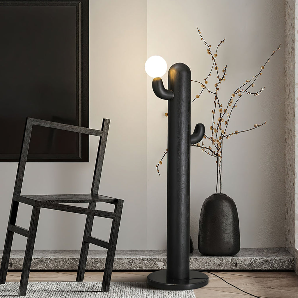Black-finished Clérachic floor lamp glows beside a dark wood chair and a vase of dried branches on a granite floor.