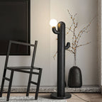 Black-finished Clérachic floor lamp glows beside a dark wood chair and a vase of dried branches on a granite floor.