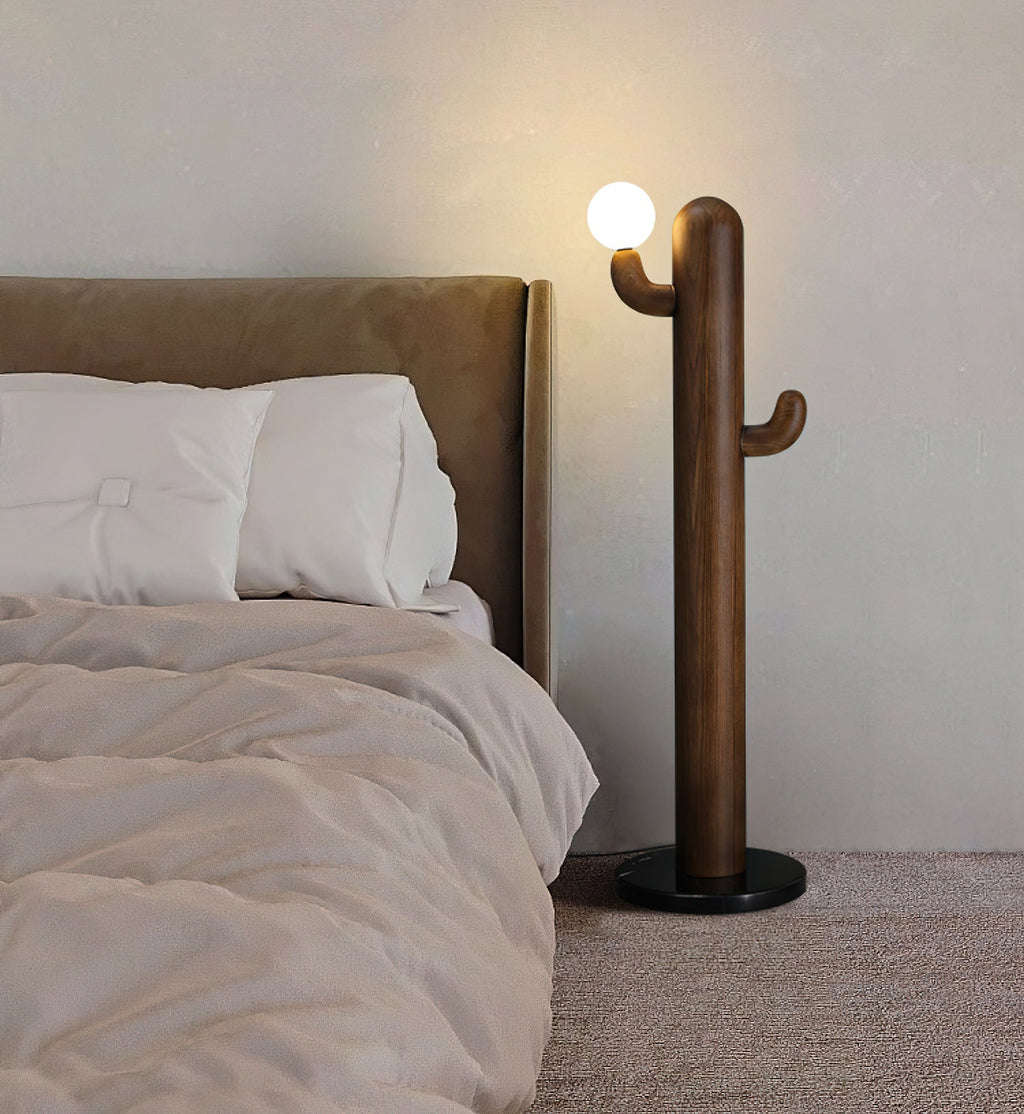 Dark wood Clérachic floor lamp glows beside a tan upholstered bed with white pillows on a soft beige rug.