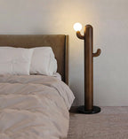 Dark wood Clérachic floor lamp glows beside a tan upholstered bed with white pillows on a soft beige rug.