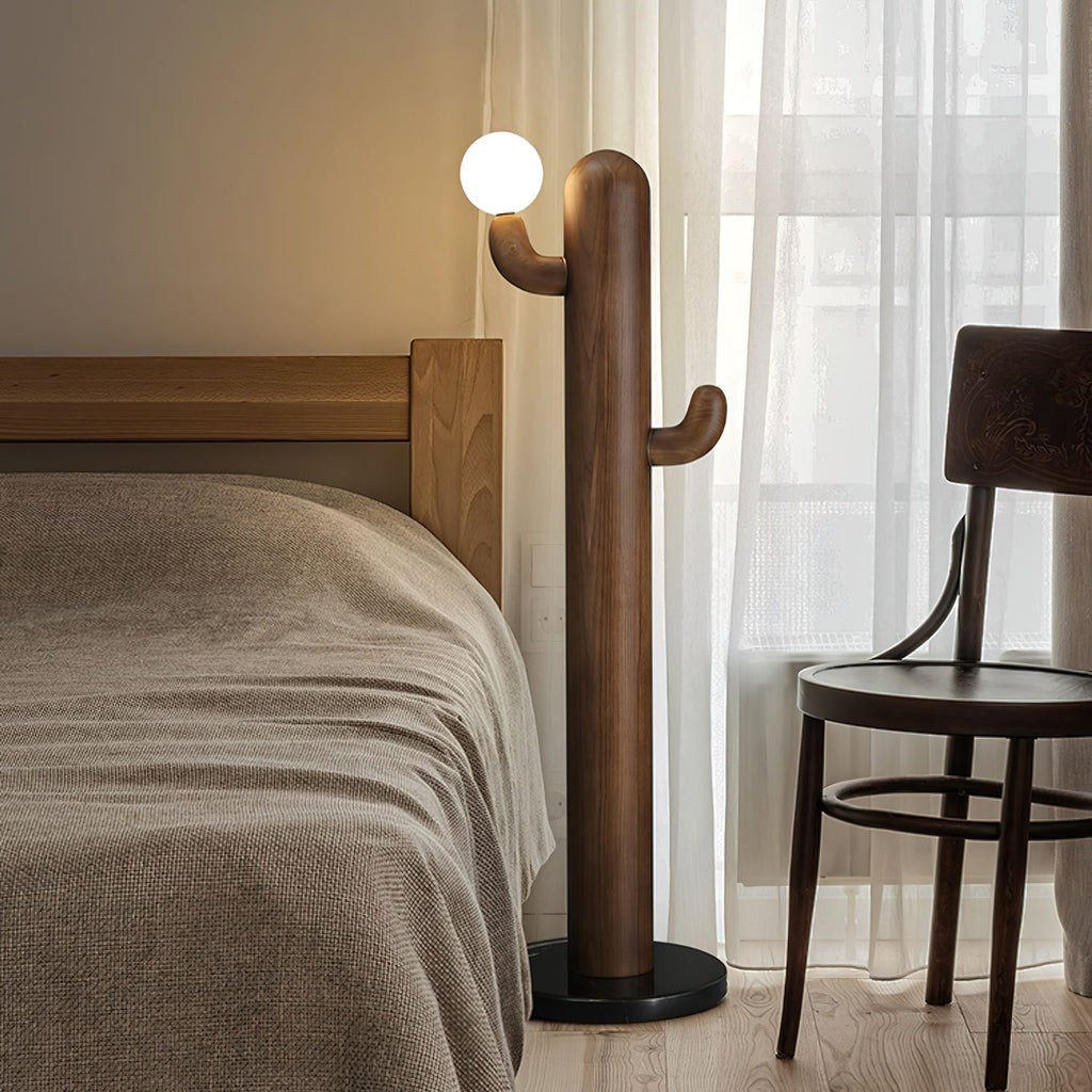 Walnut-finished Clérachic floor lamp lit beside a wooden bed frame and dark bentwood chair behind sheer curtains.