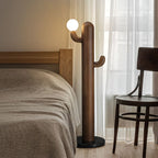 Walnut-finished Clérachic floor lamp lit beside a wooden bed frame and dark bentwood chair behind sheer curtains.