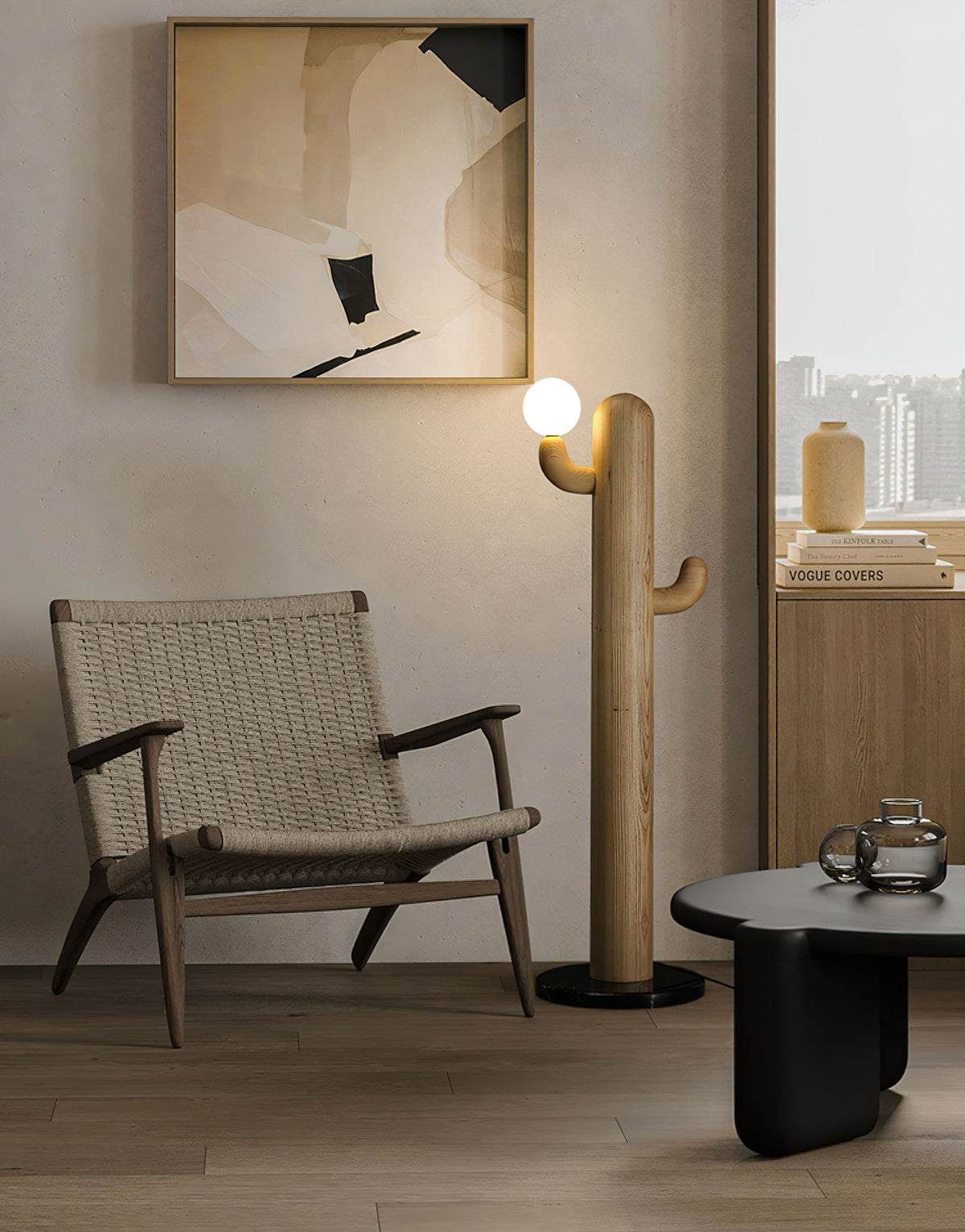 Pale-wood Clérachic floor lamp lit beside a woven lounge chair and round black coffee table under framed art.