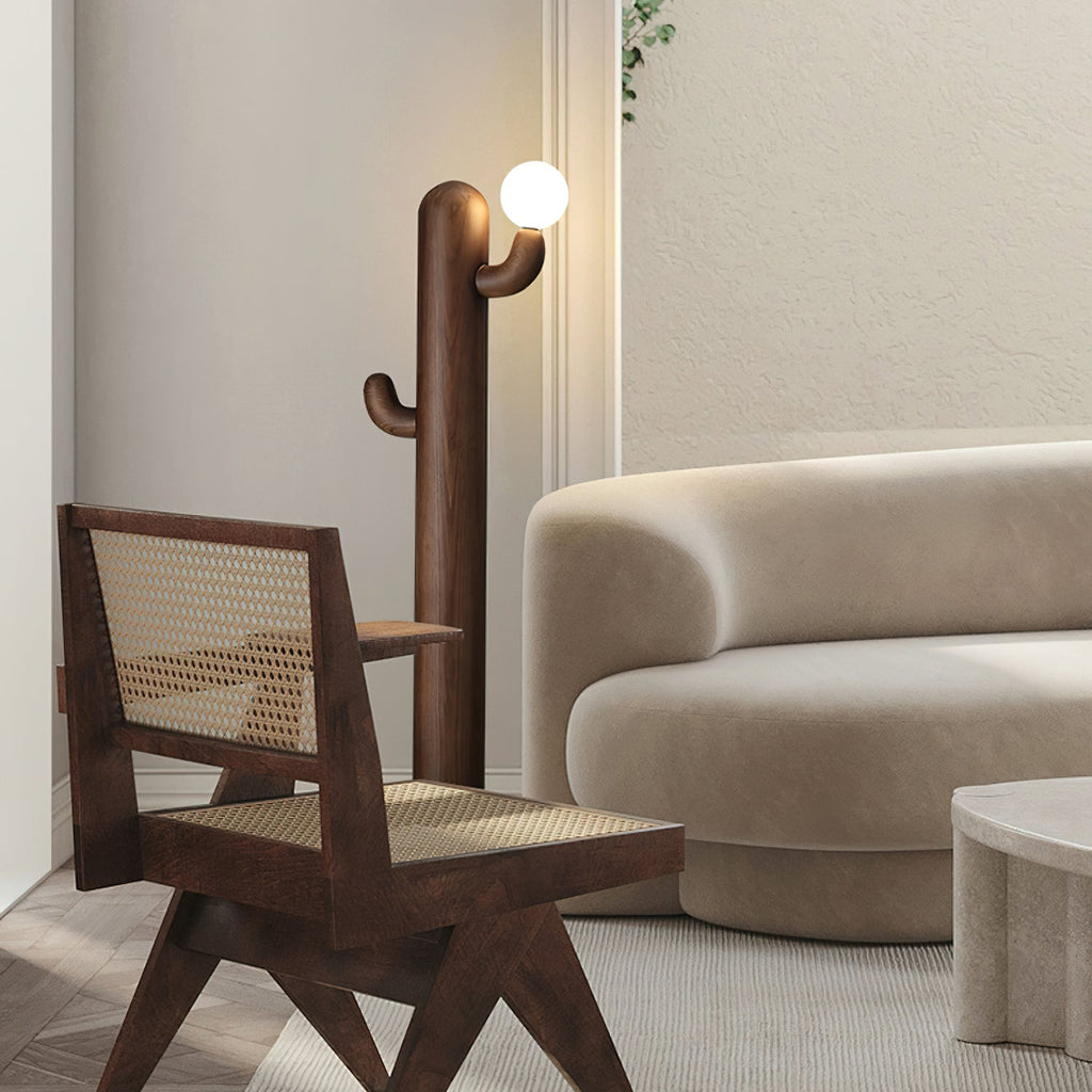 Walnut-finished Clérachic floor lamp stands lit beside a rattan-seated wood armchair and a curved cream sofa.