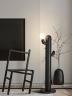Black-finished Clérachic floor lamp glows near a dark wood chair and a vase of dried branches under framed line art.