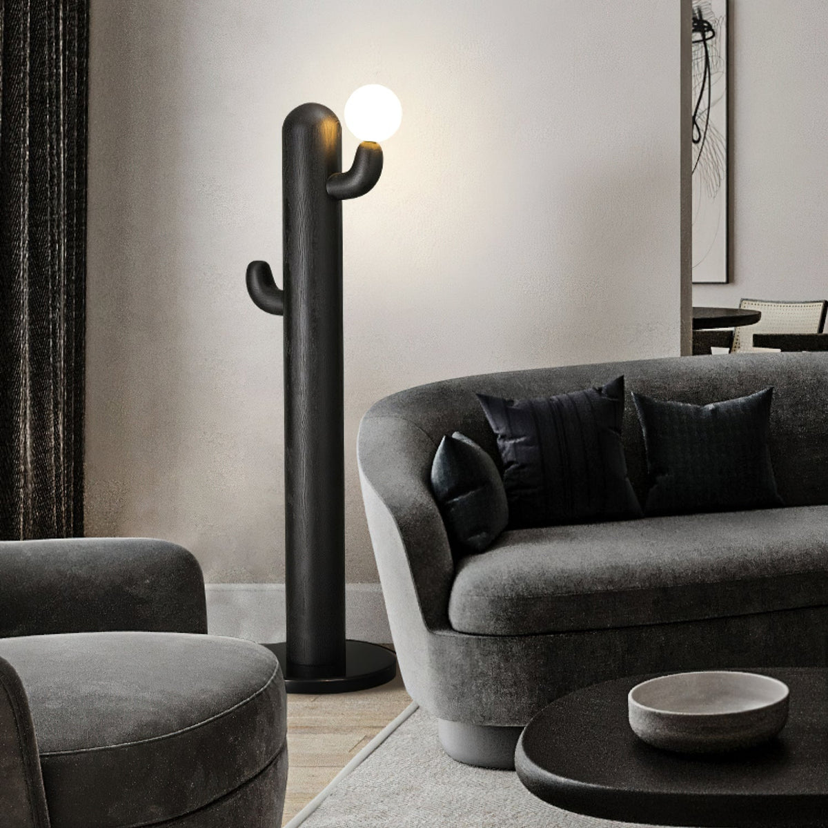 Black Clérachic floor lamp glows beside a curved grey sofa with dark pillows and a round table holding a ceramic bowl.