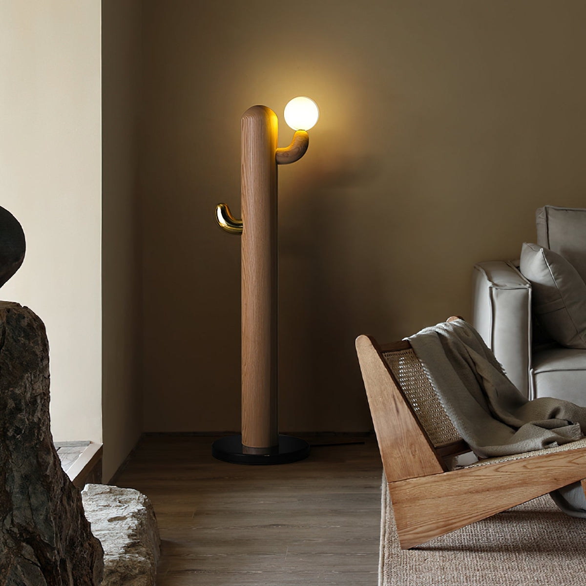 Warm walnut Clérachic floor lamp lit in a dim room corner beside a rattan lounger and a textured rock ornament.