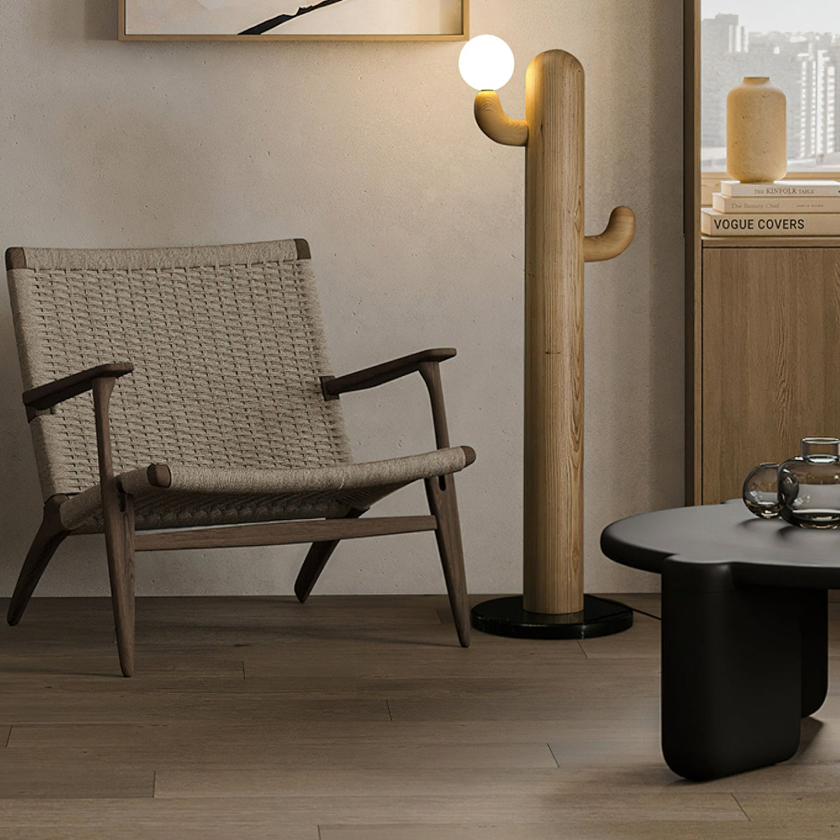 Light wood Clérachic floor lamp glows beside a woven wood armchair, a round black table and a shelf of books.