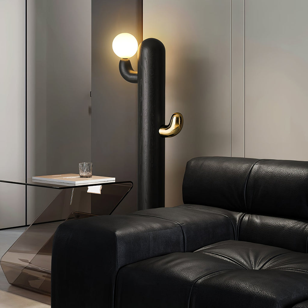 Black Clérachic floor lamp lit beside a black leather sectional and a glass-topped side table.