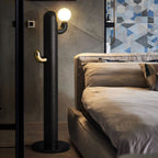 Black-finished Clérachic floor lamp glows beside a tufted leather sofa on a patterned tile floor.