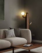 Dark wood Clérachic floor lamp lit beside a beige sofa with patterned cushions and an abstract framed print.