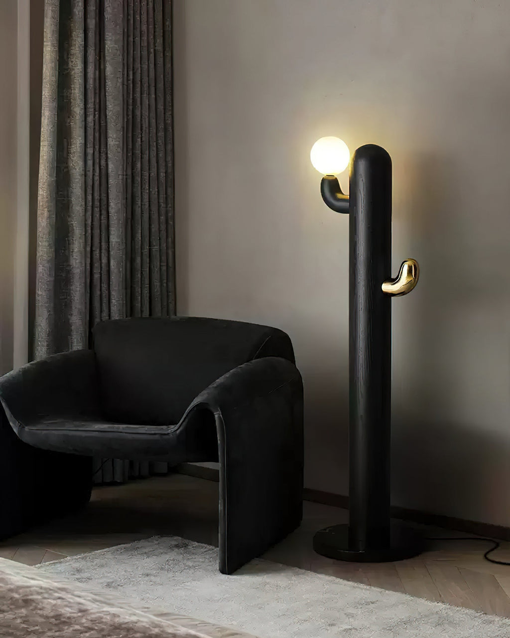 Black-finished Clérachic floor lamp lit beside a dark velvet curved armchair against a plain wall.