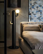 Black Clérachic floor lamp glows beside a mirrored wardrobe and a bed with neutral linens on geometric floor tile.