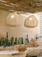 Two of this Clérachic pendant hang under a thatched pergola roof near a display of potted cacti.