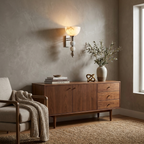 Lit beside a walnut sideboard and an upholstered armchair, this black Clérachic sconce warms a living room.